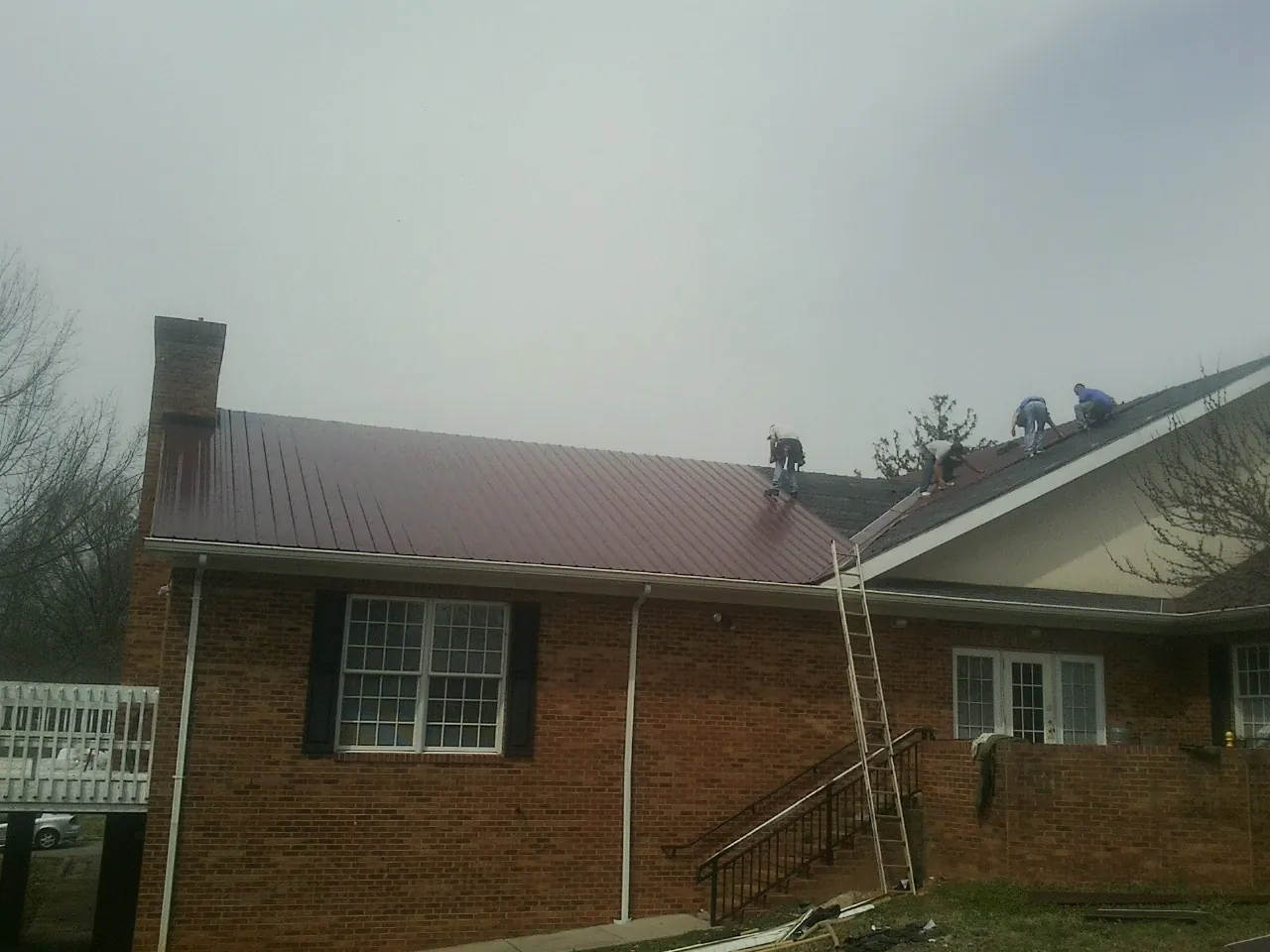 Crew setting red metal roofing panels on a brick home in Sacramento