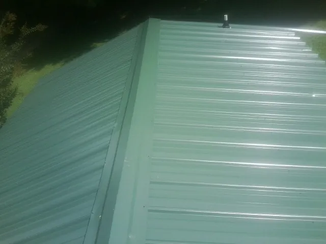 New green metal panels meeting at the ridge of a roof — Flat Roof Repair work by our crew in Sacramento