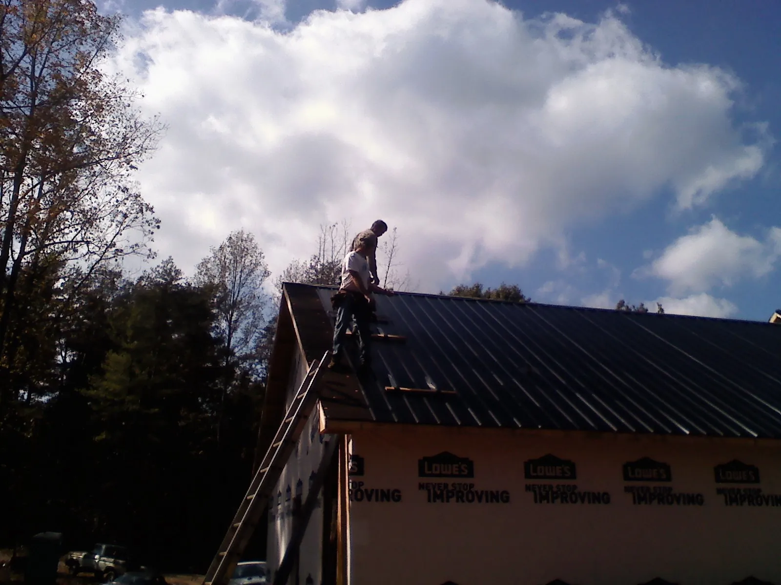 Roofer fastening dark metal panels high against a cloudy sky, from a Roof Inspection job in Sacramento